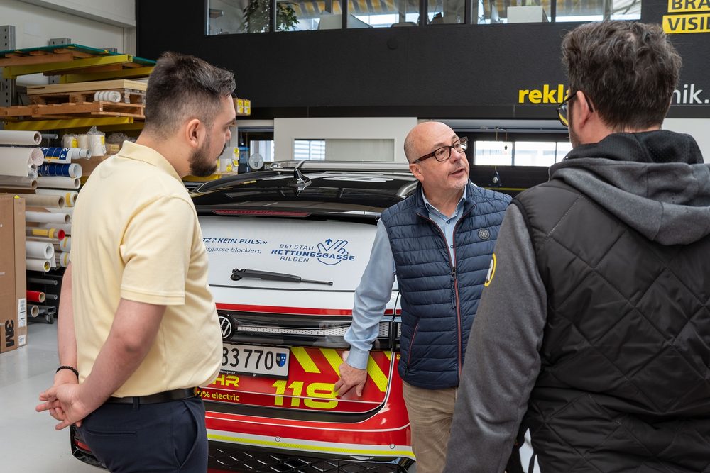 Drei Personen am Heck eines roten Feuerwehrfahrzeugs mit der Kennung 118